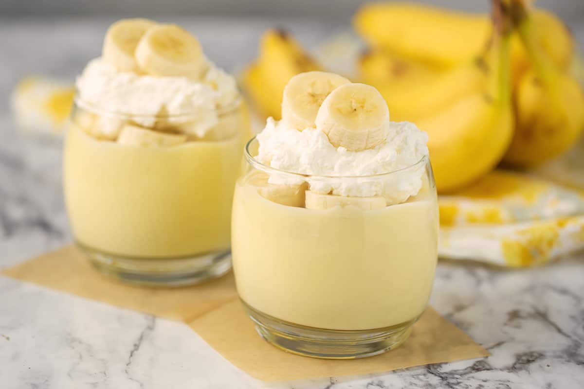 Budín de plátano en un vaso con plátanos frescos, crema batida y plátanos en el fondo