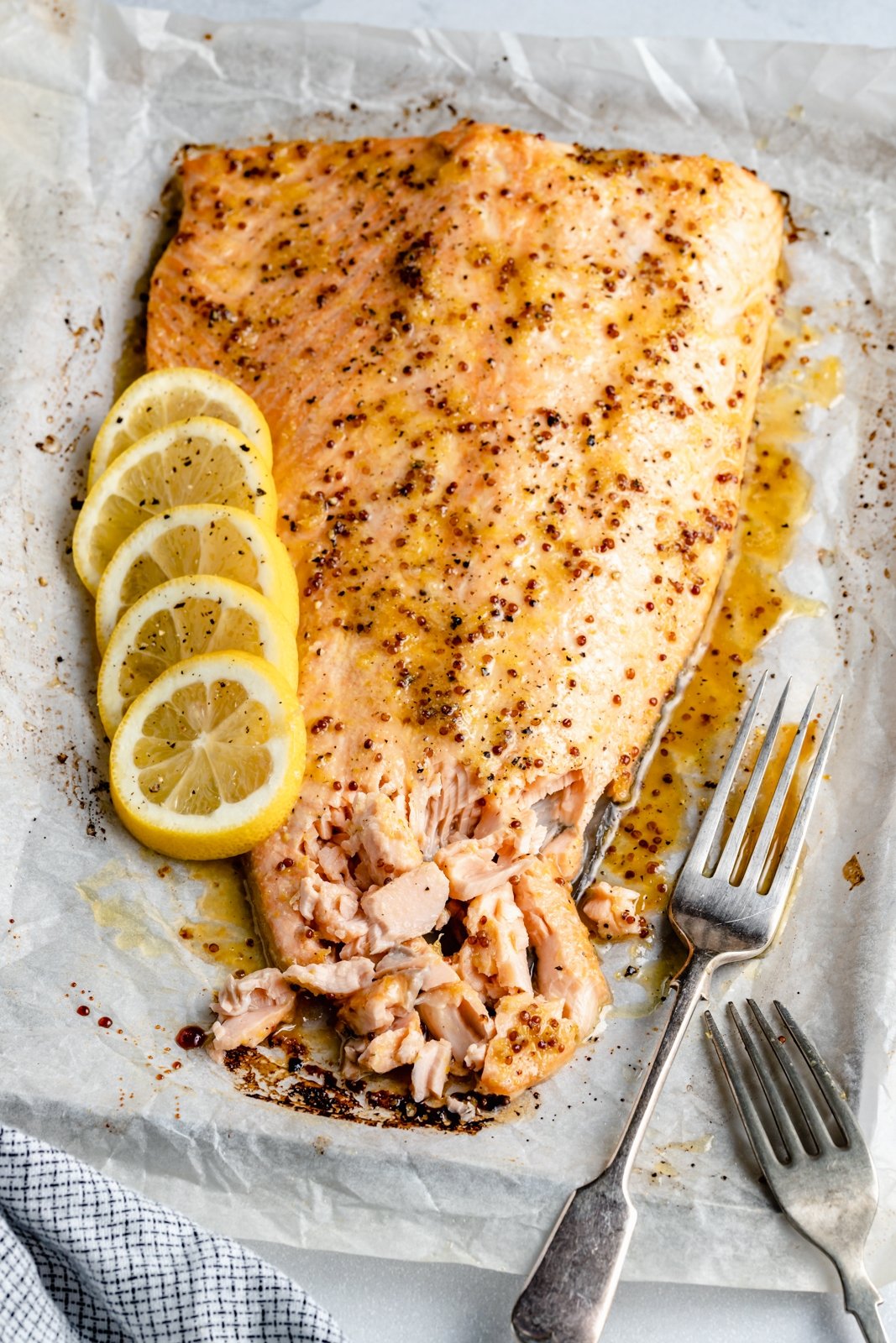 Delicioso salmón con miel de limón y ajo cubierto con un simple adobo de mantequilla de limón y ajo y hojaldre a la parrilla. Esta deliciosa receta de salmón con ajo y limón es una deliciosa cena proteica con su ensalada o guarnición favorita, y la marinada es perfecta para su proteína. Salmón a la parrilla con limón y ajo con rodajas de limón en una bandeja para hornear