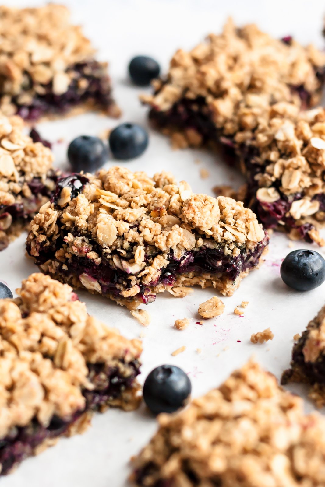 Barritas de pastel de arándanos muy dulces y saludables cubiertas con deliciosas migajas de avena. ¡Estas sencillas barritas de arándanos veganas y sin gluten saben igual que la tarta de arándanos y serán tus nuevas favoritas de primavera y verano! Tiras de arándanos en la superficie, muerde la tira del medio
