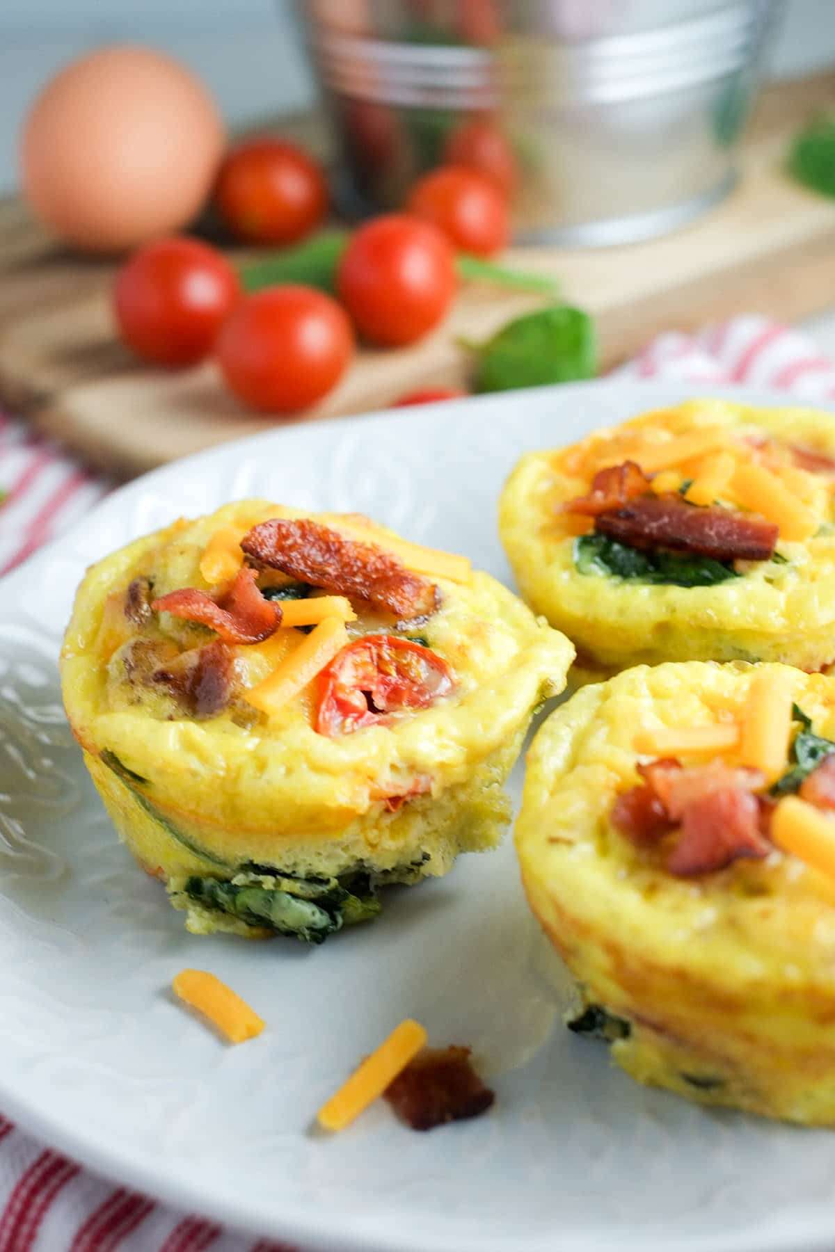 Tazas de muffin de huevo con tomates, tocino y espinacas en un plato blanco