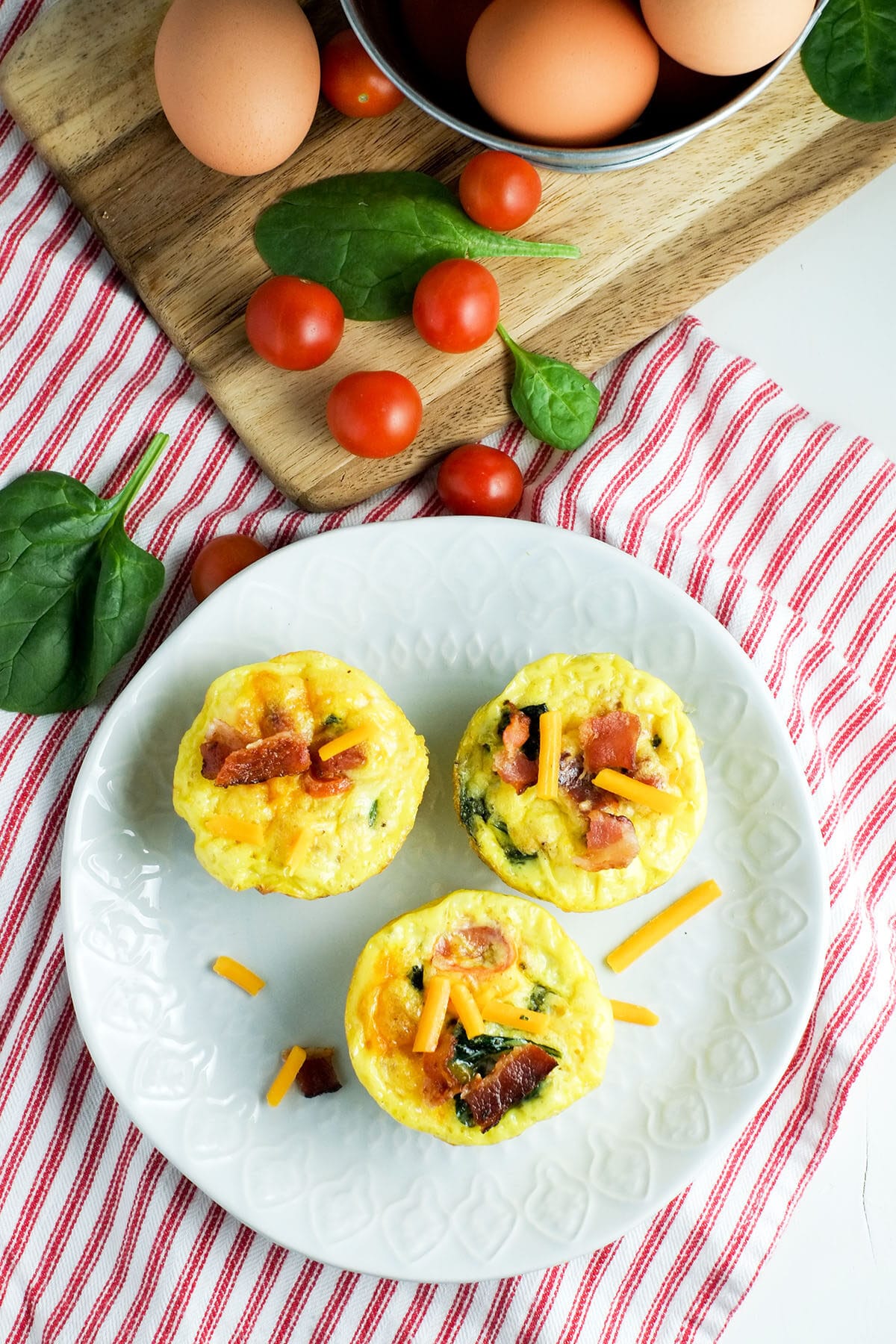 Tazas de muffin de tomate cherry, espinacas y huevo en un plato blanco con una servilleta de rayas rojas y blancas debajo