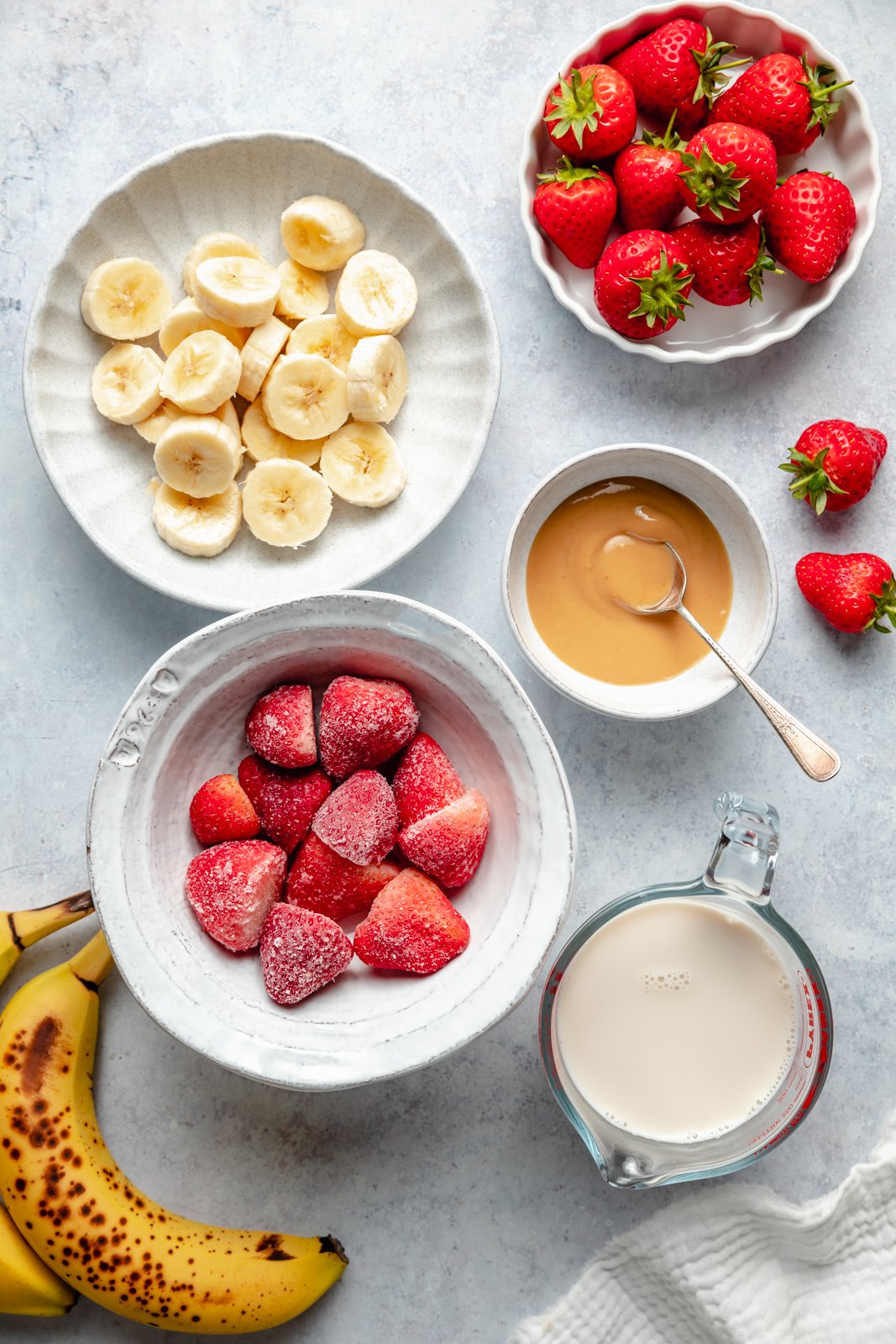 El batido de plátano, fresa y mantequilla de maní más cremoso que te deja desnudo y delicioso. ¡Solo necesitas 5 minutos y 4 ingredientes simples para hacer este increíble batido con un sabor nostálgico de plátano, mantequilla de maní y mermelada! Este batido de mantequilla de maní, plátano y fresa es vegano y está repleto de grasas saludables y proteínas, lo que lo convierte en el desayuno o merienda perfecto. Ingredientes para batido de mantequilla de maní con plátano y fresa en un tazón