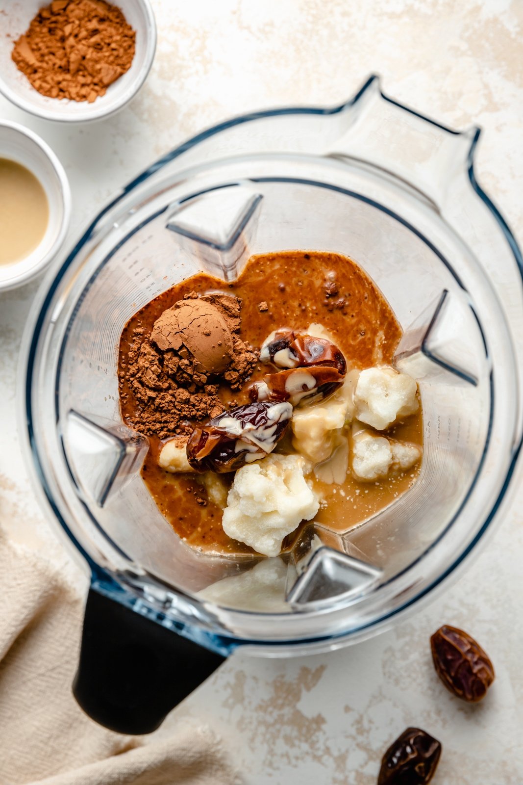 El batido de café con dátiles y tahini espeso y delicioso está hecho con leche de coco cremosa, endulzada de forma natural con dátiles. Esta receta fácil de batido de café con dátiles tiene un toque de rico sabor a cacao y chocolate e incluso contiene vegetales disimulados. Te encantará este batido por un delicioso desayuno o un refrigerio por la tarde. Vista de arriba hacia abajo de los ingredientes para el batido de dátiles de café en la licuadora