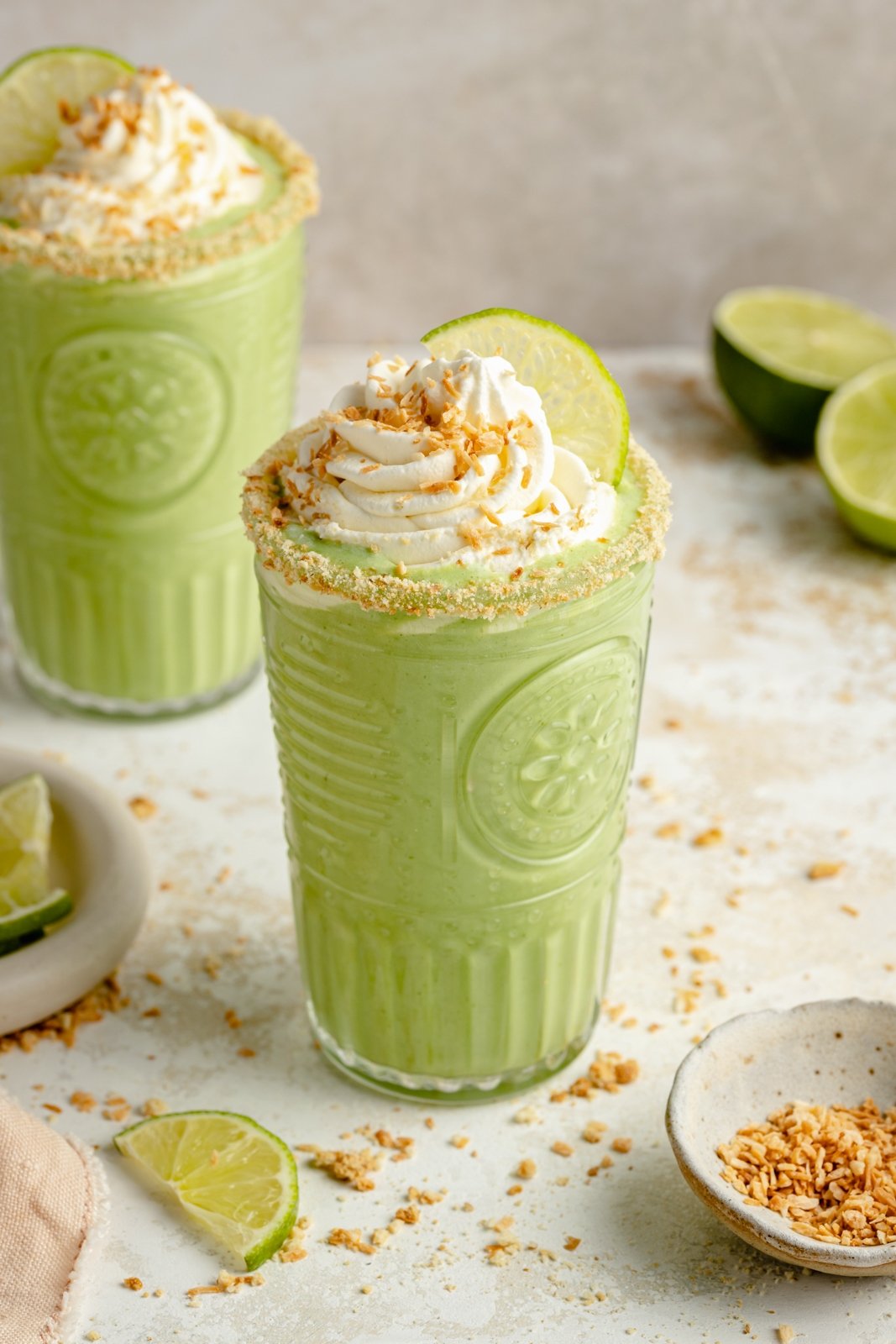 El batido cremoso de tarta de coco y lima está hecho con ingredientes simples y un delicioso sabor a coco. ¡Esta increíble receta de batido de tarta de lima sabe como una porción de tu postre favorito, pero está repleta de proteínas y vegetales disimulados! Disfruta del desayuno, la merienda o incluso el postre saludable perfecto. Batido de tarta de lima en un vaso con crema batida encima