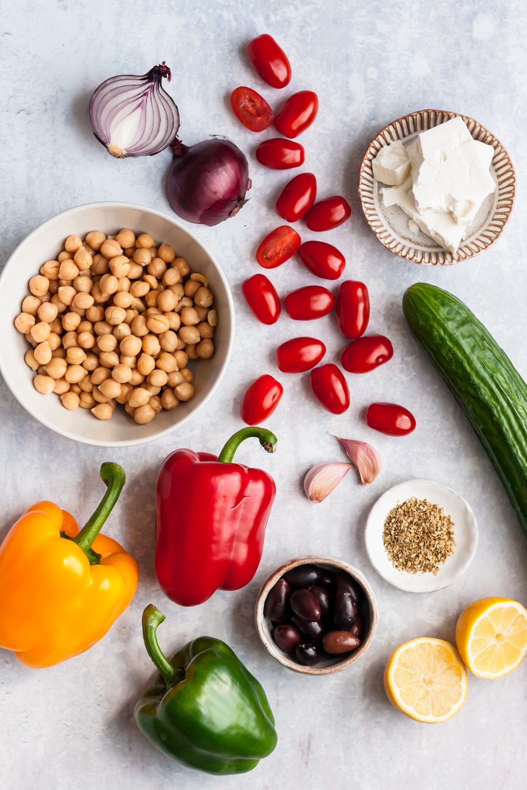 Esta receta fácil de ensalada griega picada toma menos de 20 minutos y está repleta de sabores mediterráneos, vegetales coloridos y proteína vegetal de garbanzos. Te encantará esta ensalada griega de garbanzos porque es rápida y fácil para el almuerzo o para tomar ¡a una fiesta! Ingredientes para ensalada de garbanzos griegos en superficie gris