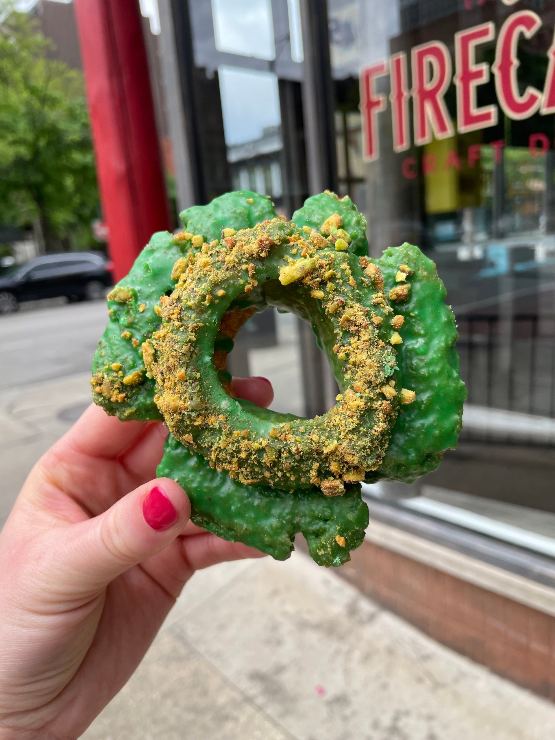¡Es hora de enfrentarse a su gusto por lo dulce con las mejores donas de Chicago! En nuestra próxima guía de la serie Ambitious Kitchen Chicago, encuestamos a nuestra audiencia y exploramos la ciudad. Encuentre las mejores donas y tiendas de donas. Estará buscando Sabores deliciosos y únicos para crear el regalo perfecto que sorprenderá a los invitados de fuera de la ciudad. Sosteniendo una dona verde frente a una tienda de donas en Chicago