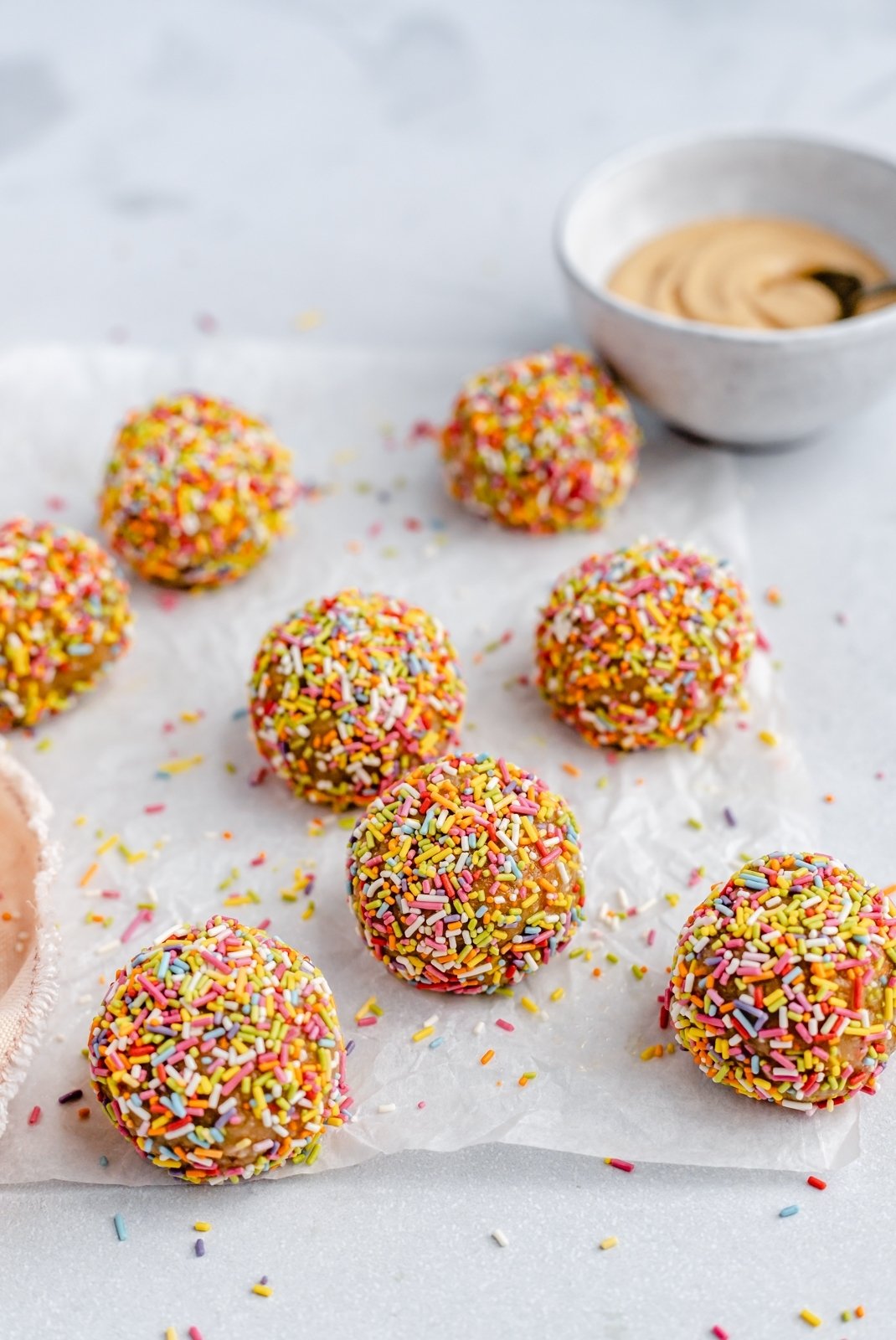 ¡No hornee picaduras de energía de masa de galleta de pastel de cumpleaños que saben igual que la masa de pastel! Hechos con siete ingredientes simples, estos refrigerios veganos energéticos fáciles de pastel de cumpleaños están endulzados naturalmente con jarabe de arce puro y rellenos con chispas festivas. ¡El tentempié o tentempié repleto de proteínas perfecto! Bolas energéticas de pastel de cumpleaños vegano en pergamino