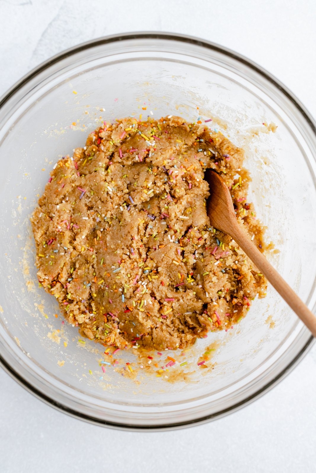 ¡No hornee refrigerios energéticos de masa de galleta de pastel de cumpleaños que saben igual que la masa de pastel! Estos refrigerios veganos fáciles de energía de pastel de cumpleaños están hechos con siete ingredientes simples, endulzados naturalmente con jarabe de arce puro y rellenos con chispas festivas. ¡merienda o golosina! Mordeduras de energía de masa de pastel de cumpleaños en un tazón