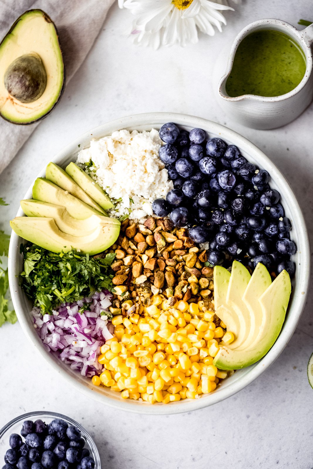 Magnífica ensalada de aguacate, arándanos y quinua con maíz fresco, cebolla roja, queso feta picante, pistachos picados y mezclada con un delicioso aderezo de cilantro y lima. Esta deliciosa ensalada vegana de quinua es perfecta para almuerzos de verano, fiestas y comidas al aire libre. Maíz, arándanos, quinua, queso feta, aguacate, cebolla roja, pistachos y cilantro en un bol