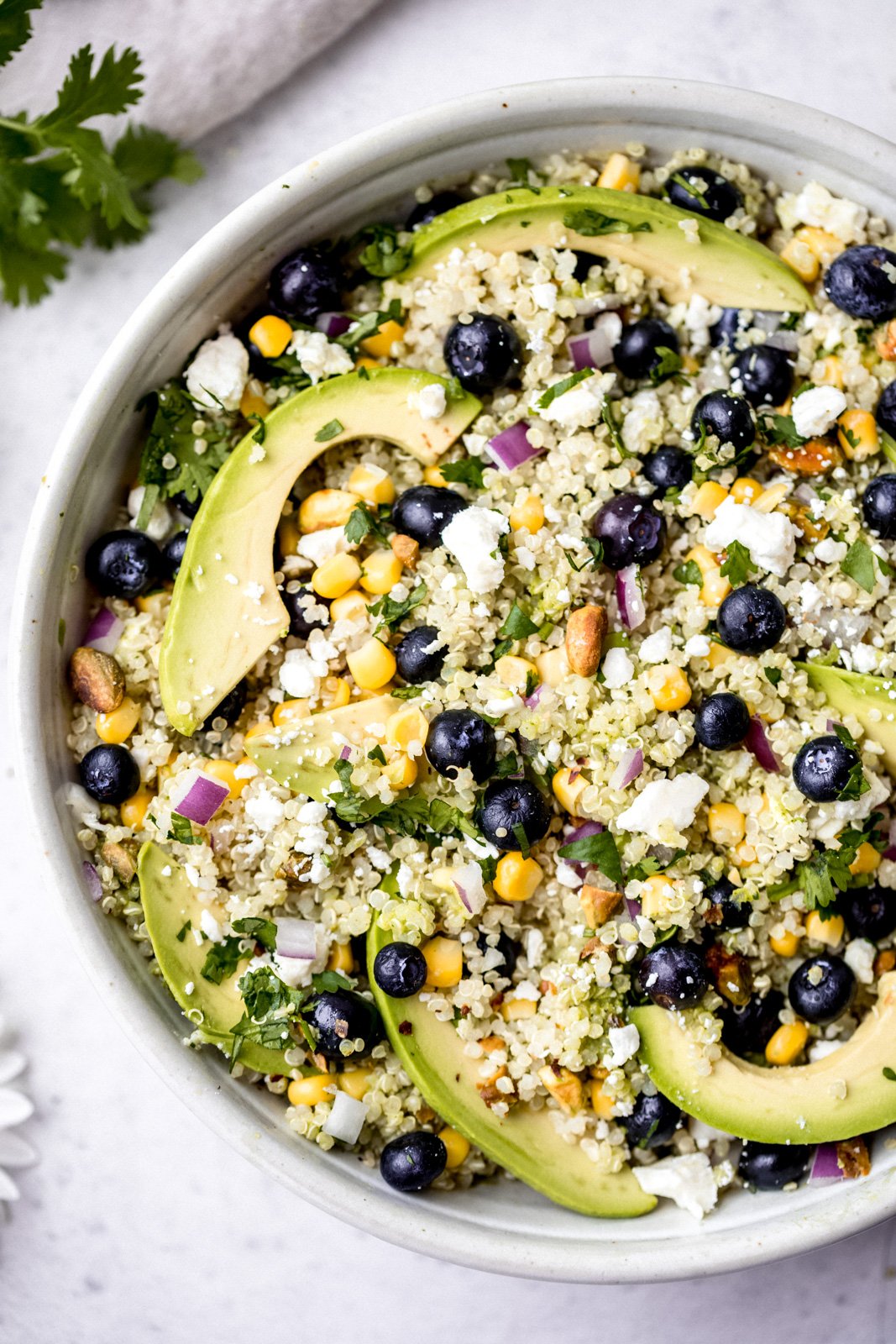Magnífica ensalada de aguacate, arándanos y quinua con maíz fresco, cebolla roja, queso feta picante, pistachos picados y mezclada con un delicioso aderezo de cilantro y lima. Esta deliciosa ensalada vegana de quinua es perfecta para almuerzos de verano, fiestas y comidas al aire libre. Ensalada De Aguacate, Arándanos Y Quinoa En Un Tazón