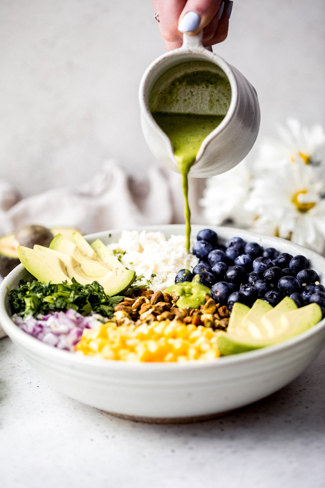 Magnífica ensalada de aguacate, arándanos y quinua con maíz fresco, cebolla roja, queso feta picante, pistachos picados y mezclada con un delicioso aderezo de cilantro y lima. Esta deliciosa ensalada vegana de quinua es perfecta para almuerzos de verano, fiestas y comidas al aire libre. Vierta el aderezo sobre la ensalada de aguacate, arándanos y quinua.