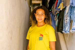 Vit?ria La?s de Souza Gomes, 15, residente de Mar?, en la entrada de su apartamento, con su camiseta amarilla? ¿ella? ¿Es anti-dengue? - Español: Héroes contra el Dengue.