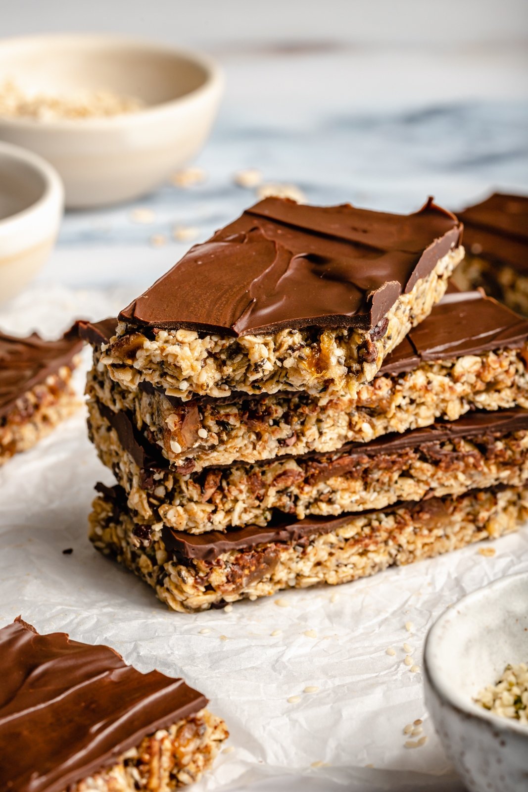 Barras nutritivas de avena con tahini rellenas con semillas de chía, semillas de cáñamo y copos de avena, endulzadas de forma natural con higos secos y miel. Estas sencillas barritas sin hornear están cargadas de fibra y proteína para mantenerte lleno y satisfecho. Rocía con un delicioso chocolate y ¡disfruta de la merienda perfecta o delicia recién sacada de la nevera!” src= Barras de avena Tahini en una pila