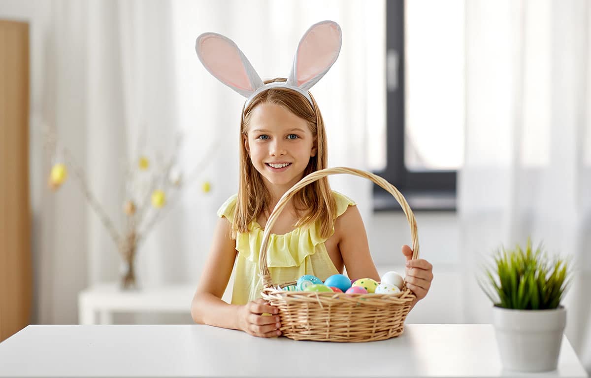 Semana Santa, vacaciones y concepto de la gente - chica feliz en diadema con orejas de conejo con cesta de huevos pintados en casa