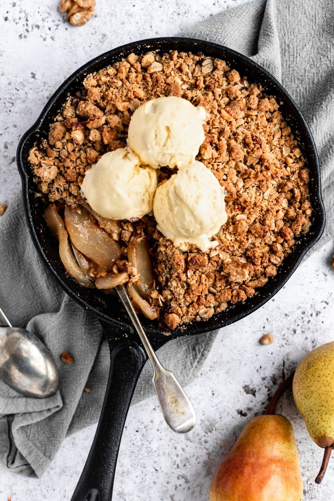 healthy pear crisp in a skillet topped with ice cream