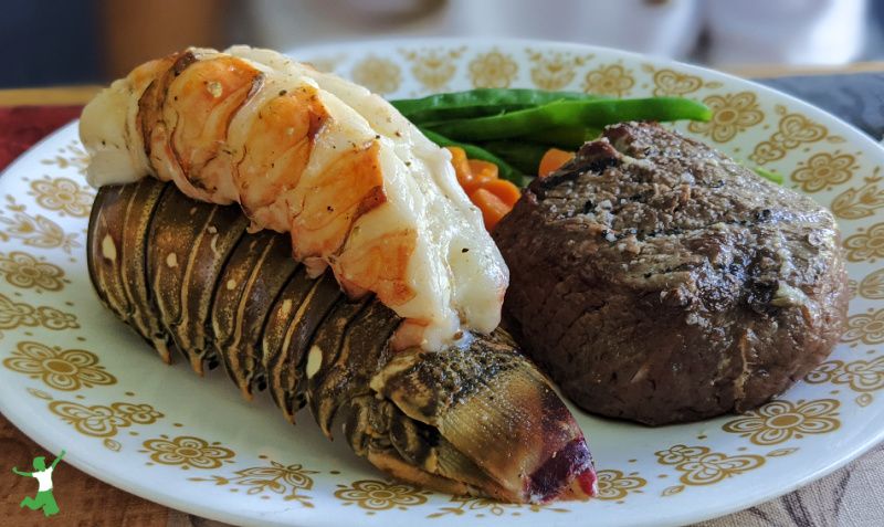 baked Florida lobster tail with filet and vegetables on a white plate