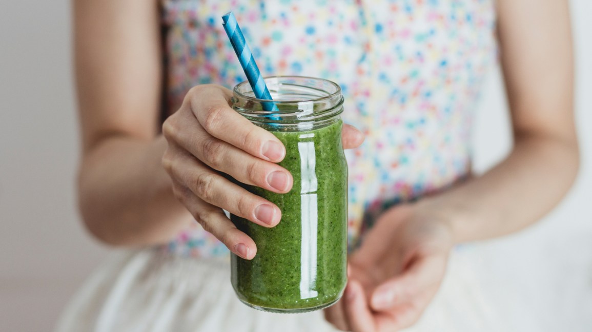 child holding green smoothie with straw