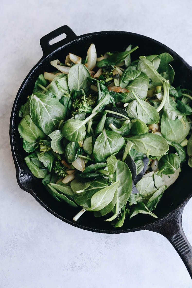 Agregue las espinacas, la cebolla y el brócoli a la sartén de hierro fundido antes de saltear.