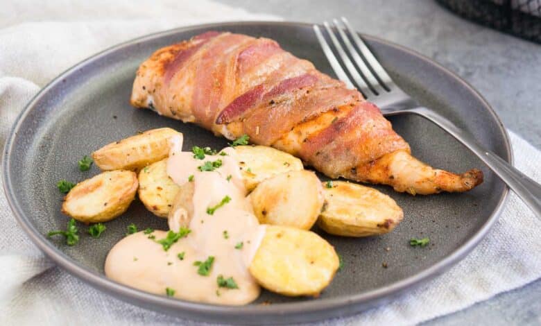 close up image of chicken wrapped in bacon with roasted potatoes on a plate