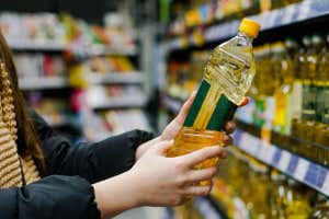 2HKYX4G Mujer elige aceite de girasol en supermercado. Primer plano de una mano sosteniendo una botella de aceite en la tienda.