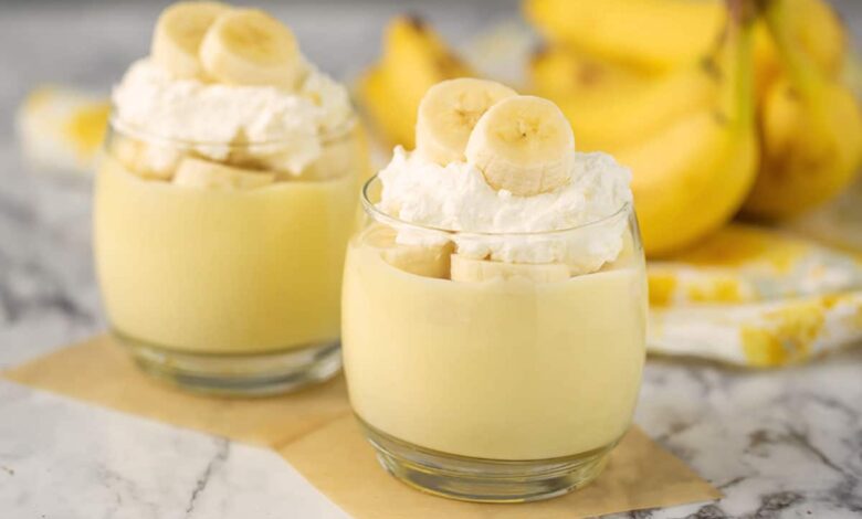 banana pudding in glasses with fresh bananas, whip cream and bananas in the background