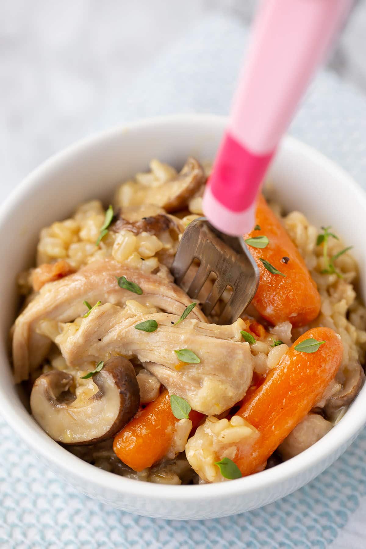 Instant Pot Chicken and Brown Rice con pollo, champiñones, zanahorias y arroz integral en un tazón blanco con un tenedor rosa
