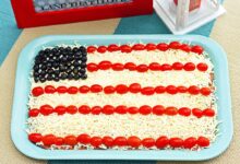 layered bean dip that looks like an american flag with tomatoes, mozzarella cheese and olives