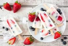Healthy strawberry blueberry yogurt popsicles on a plate, above view summer table scene against a white wood background