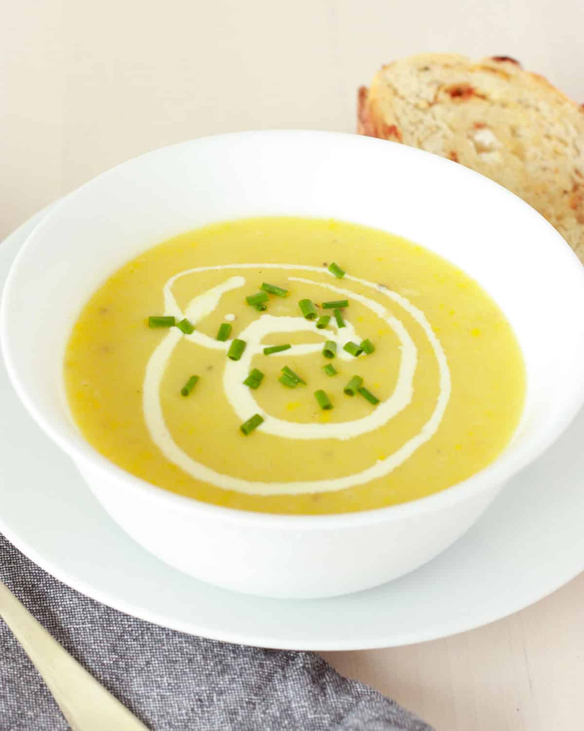 Sopa cremosa de calabaza amarilla servida con cuchara de metal y pan de masa madre con puerros verdes como guarnición