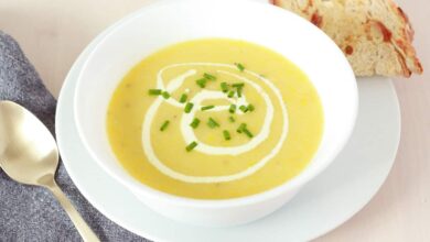 creamy yellow squash soup with a metal spoon and sourdough bread on the sides, green chives on top as a garnish