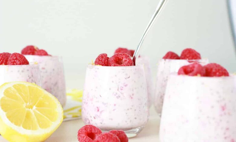lemon raspberry chia seed pudding in small glass jars with fresh raspberries and lemon zest on top with a small silver spoon in the jar and a fresh lemon in the background