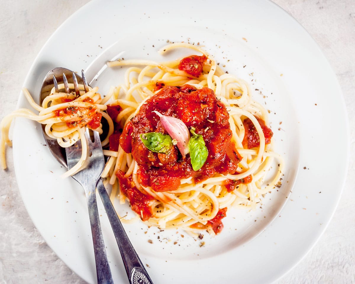 Una porción de pasta con salsa de pasta de tomate y albahaca sobre una mesa de hormigón blanco.