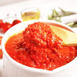 La salsa espesa de pasta de tomate se coloca en una sartén blanca, use una cuchara de madera para quitar la salsa de la sartén.