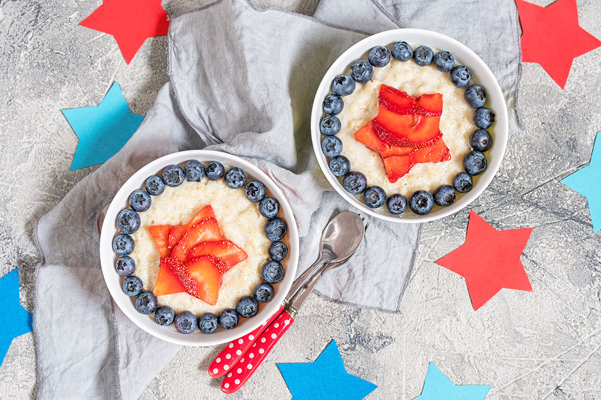 Crema de trigo, fresas y arándanos en un bol con un patrón de estrella patriótico sobre un fondo de cucharas de lunares rojos y estrellas cortadas en papel