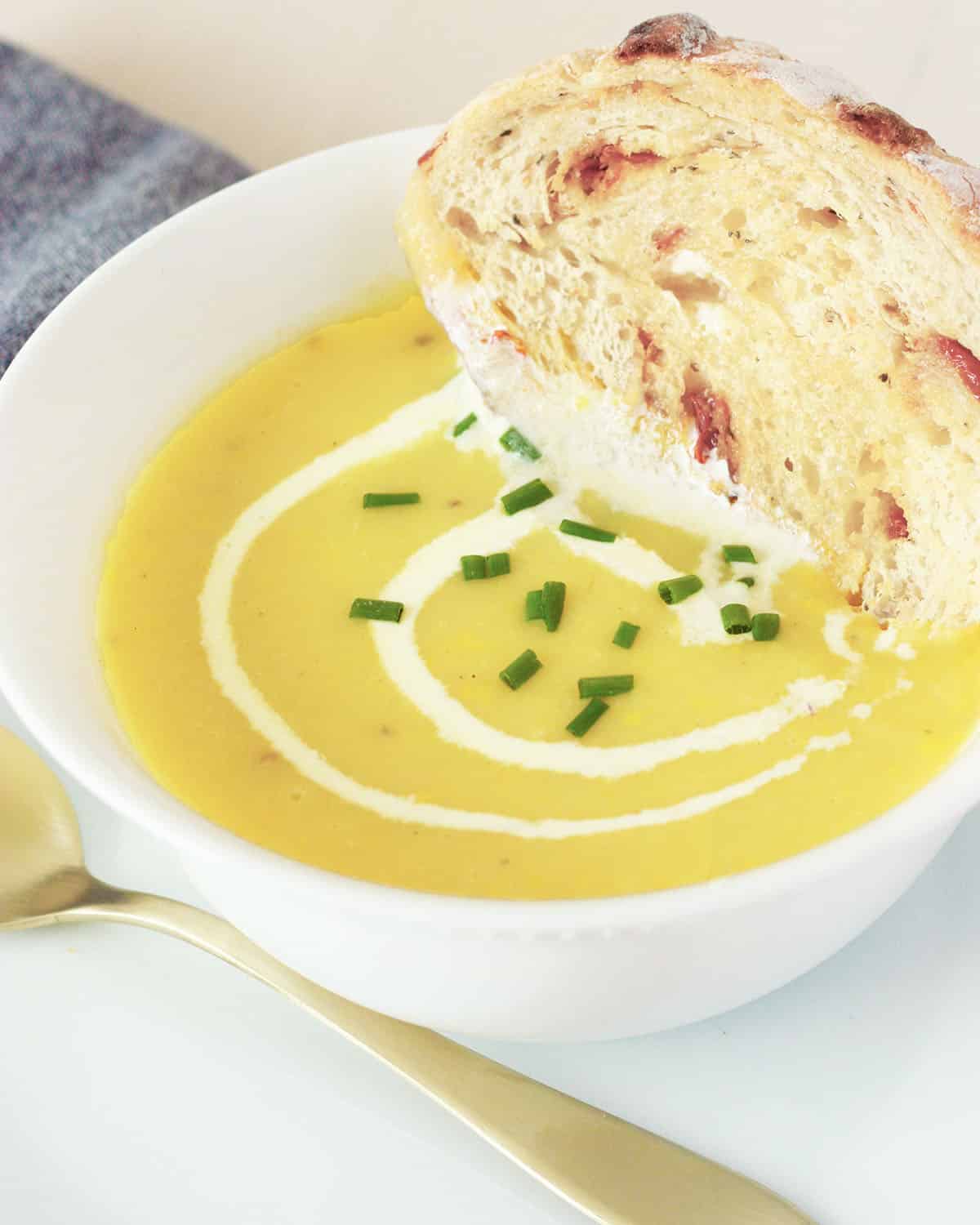 Un bol de sopa de calabaza amarilla bañada en pan de masa madre, puerros como guarnición y un remolino de nata