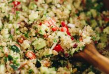 cucumbers, tomatoes, red onion, parsley and white quinoa mixed together in a brown bowl.