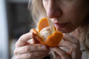 Mujer enferma tratando de oler naranjas frescas, con síntomas de Covid-19, infección por coronavirus - perdiendo el sentido del olfato y el gusto, de pie en casa. Uno de los principales síntomas de la enfermedad. Existe ID de Shutterstock 1898515471; Orden de compra: -; Trabajo: -; Cliente: -; Otro: -