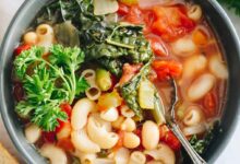 Minestrone soup recipe overhead in a blue bowl with kale and parsley on top.