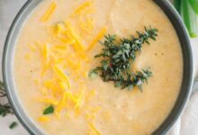 roasted cauliflower soup in a blue bowl topped with fresh thyme and cheddar cheese.