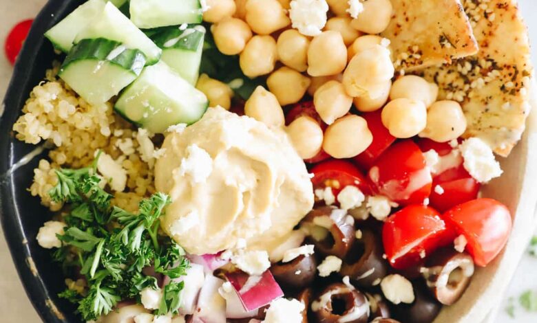 overhead photo of a mediterranean quinoa bowl with pita chips, hummus, tomatoes, cucumbers, red onion and olives.