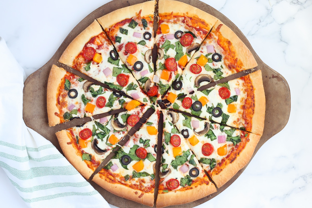 Pizza de verduras en rodajas sobre piedra de pizza con lino de rayas verdes.