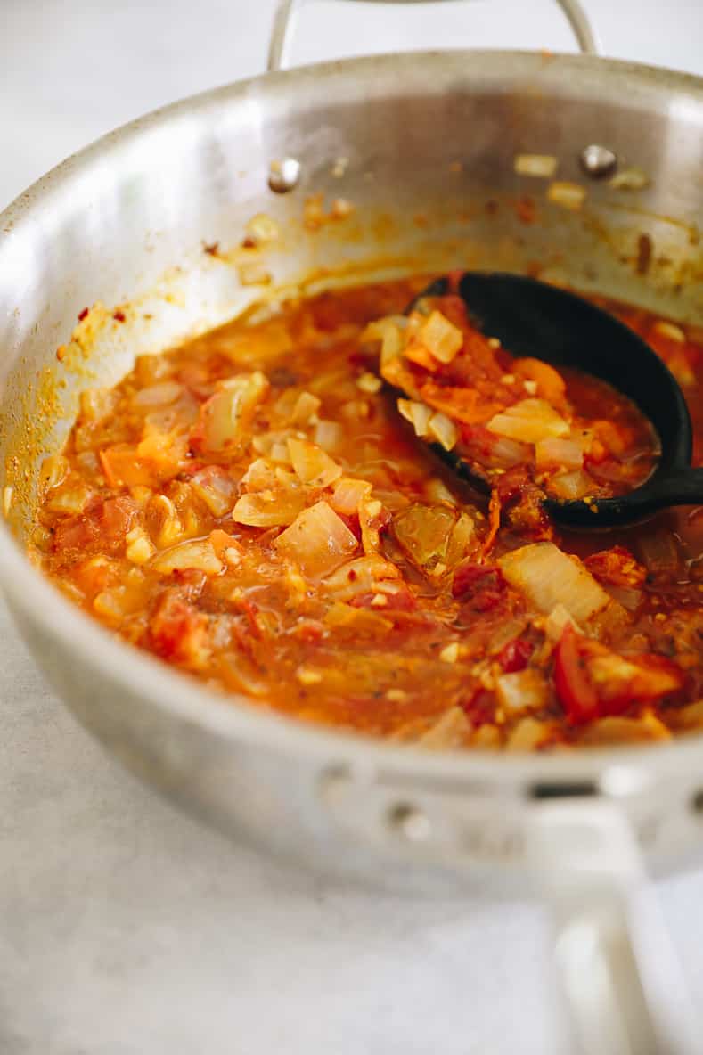 Cocinar tomates, cebollas y ajo en una olla grande para hacer salsa arrabiata casera.