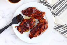 Grilled BBQ Chicken Breasts on a white plate with a pastry brush and a striped linen in the background.