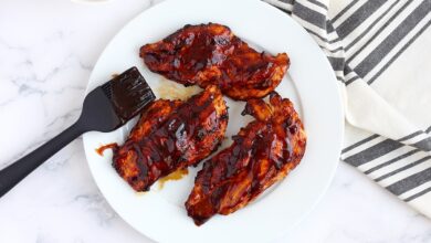 Grilled BBQ Chicken Breasts on a white plate with a pastry brush and a striped linen in the background.