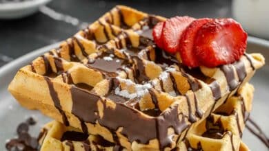 waffles on a plate drizzled with chocolate and topped with sliced strawberry