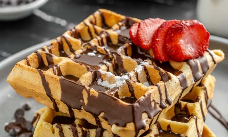 waffles on a plate drizzled with chocolate and topped with sliced strawberry