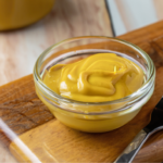 aderezo de ensalada de mostaza y miel en un recipiente de vidrio sobre una tabla de cortar de madera con un tenedor